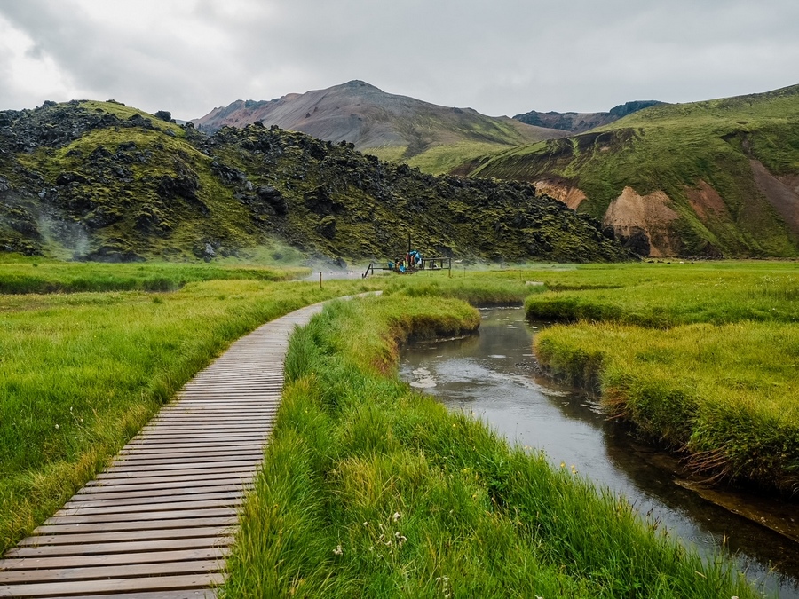 在冰岛Landmannalaugar露营地，一群游客在温泉浴中放松，通往天然温泉的木制小径